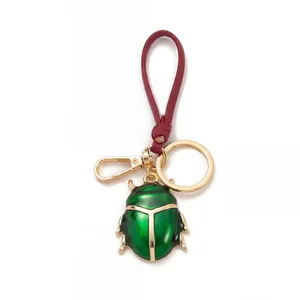 Portachiavi scarabeo verde con cinturino in pelle rossa e dettagli dorati eleganti.
