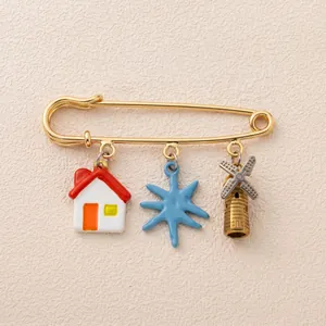 Close-up of gold safety pin brooch with house, star, and windmill charms