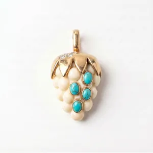 Détail macro d'un pendentif en forme de fruit doré avec turquoises et perles blanches