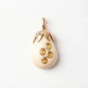 Gros plan macro d'un pendentif fruit en or avec corps crème et quatre pierres précieuses jaunes.
