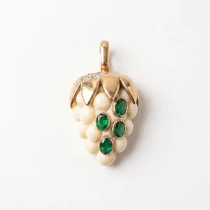 Détail d'un pendentif en forme de fraise avec feuilles d'or et pierres vert émeraude