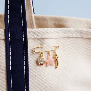 Detail shot of a gold-plated safety pin brooch with three stylish hanging charms.