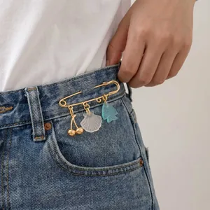 Close-up of gold safety pin brooch with cherry, shell, and fish charms on denim jeans