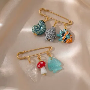 Detail view of gold-plated safety pin brooches with ocean animal and mushroom charms
