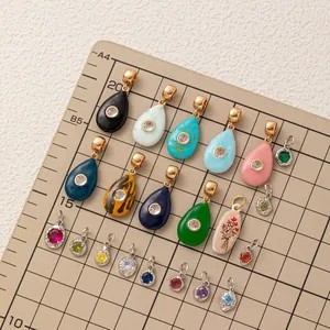 Various colorful teardrop and round jewelry charms on a grid measurement board.