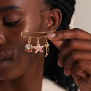 Detail view of a gold-plated safety pin brooch featuring ship, star, and horn charms