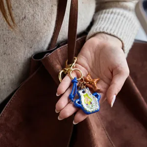 Close-up of hand-painted blue pot and starfish bag charms attached to a brown suede bag