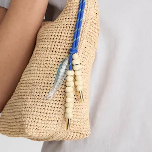 Macro detail of a light blue fish pendant and beige beads on a woven straw bag accessory