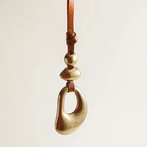 Close-up of artistic vintage bronze-tone metal charm with brown knotted leather strap.