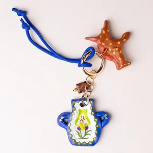 Artisanal hand-painted blue vase and star-shaped bag charm with vibrant cord and gold clasp