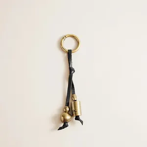 Vintage brass bell and leather cord keychain detail showing antique finish textures