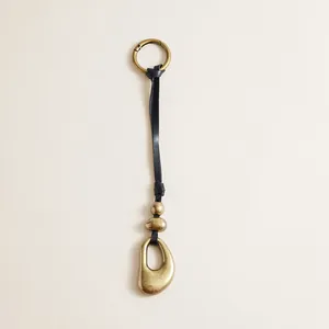 Macro detail of vintage leather strap bag charm featuring antique brass finish metal pendants