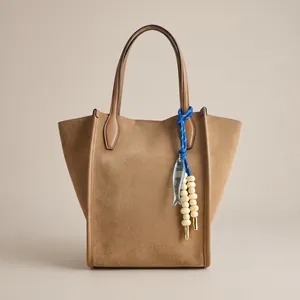 Detailed view of brown suede tote bag with artistic blue fish rope charm accessory