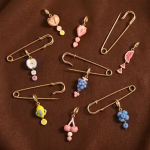 Gros plan de pendentifs en émail aux fruits et d'épingles dorées sur un tissu marron texturé