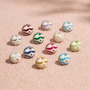 Macro view of twelve birthstone copper charms with colorful wavy enamel stripes on sand