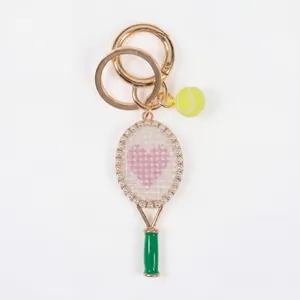 Detail eines goldenen Tennisschläger-Schlüsselanhängers mit Herz und Perlen.