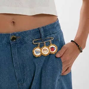 Detail van een gouden veiligheidsspeld broche met koffie- en theekopjes op een spijkerbroek