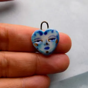 Gros plan d'un pendentif en porcelaine émaillée bleue en forme de cœur avec visage.