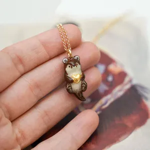 Detailed close-up of a handcrafted ceramic otter pendant holding a gold heart on a fine chain