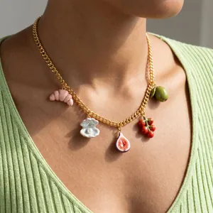 Détail d'un collier doré de style nordique avec des breloques de fruits et croissants