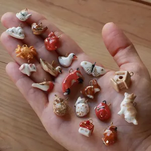 Main tenant divers mini pendentifs en céramique d'animaux, notamment renard, canard et lapin