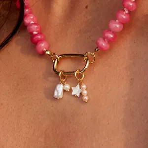 Détail d'un collier avec des perles roses, un lien mousqueton doré et des breloques étoiles