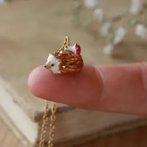 Macro détaillée d'un minuscule pendentif hérisson avec champignon sur le bout d'un doigt.