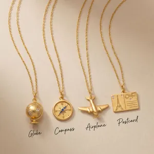 Detailansicht von vier goldenen Anhängern: Globus, Kompass, Flugzeug und Postkarte für Reisen.