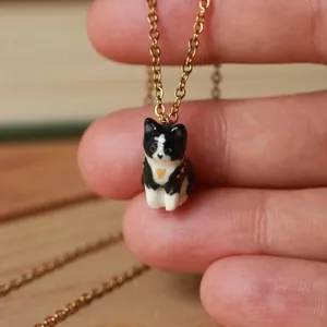 Détail d'un collier pendentif chat tuxedo fait main sur une chaîne dorée très élégante