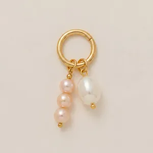 Gros plan d'un pendentif anneau doré avec perles roses et blanches sur fond beige