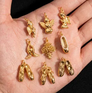 Detailed view of gold-plated angel and ballet shoe pendants on a hand for scale