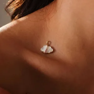 Detailopname van een iriserende wolkvormige gouden hanger met roze steentjes op de huid