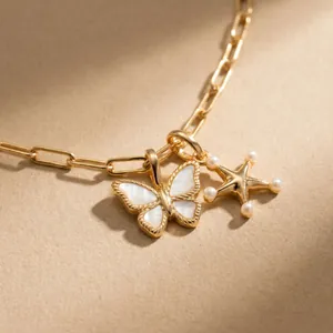 Close-up detail of 18K gold-plated butterfly shell charm and pearl star pendant.