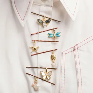 Detailed view of nature-themed gold charms on a white shirt with red stitching