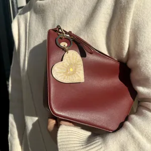 Creative heart-shaped acrylic bag charm with sun eye motif shown on burgundy bag