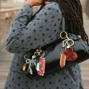 Creative acrylic bag charms with car, heart and bow shapes on black handbag.