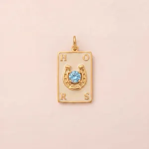 Détail d'un pendentif fer à cheval doré avec zircon bleu et lettres gravées style chic.