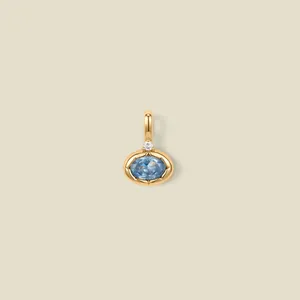 Macro detail of a 18K gold-plated oval pendant featuring a faceted light blue gemstone
