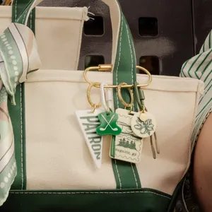 Close-up of decorative bag charms with lotus and golf themes on a canvas tote