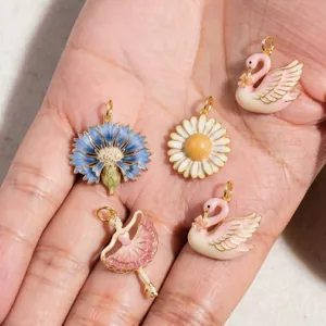 Detailed view of delicate enamel ballet dancer and swan pendants held in hand.