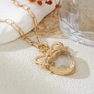 Vue détaillée d'un collier cœur doré avec nœud papillon et insert en verre transparent