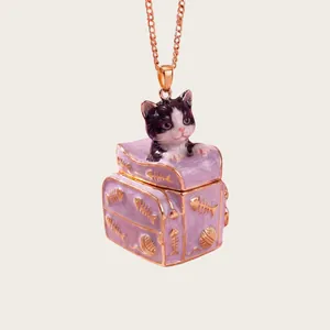 Close-up of a pink enamel kitten trunk pendant necklace with gold fish bone details.