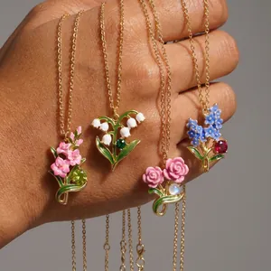Hand holding four elegant enamel flower necklaces with colorful birthstone accents