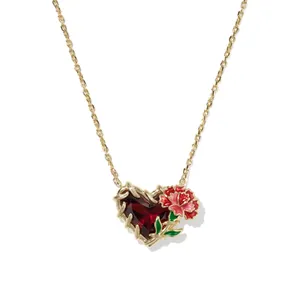 Makroansicht einer vergoldeten Herzkette mit rotem Edelstein und Emaille-Blumendetail