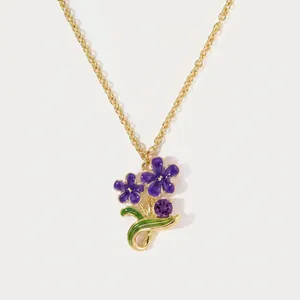 Detailed close-up of a purple enamel flower pendant on a dainty gold chain necklace.