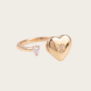 Vista detallada de un anillo de relicario de corazón dorado con circonitas.