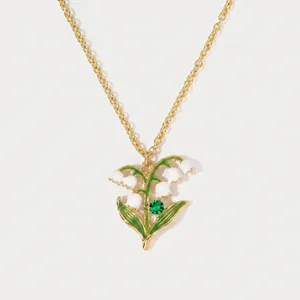 Detail view of gold-tone lily of the valley enamel pendant with green crystal accent