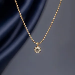 Macro detail view of elegant gold bead chain necklace with round bezel-set sparkling pendant