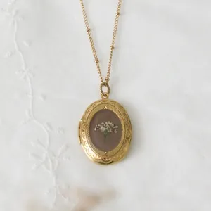 Nahaufnahme eines goldenen Medaillons mit echten weißen Trockenblumen im Vintage-Stil