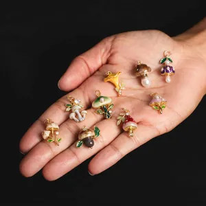 Detailed view of colorful mushroom charms with enamel and pearl accents held in palm.